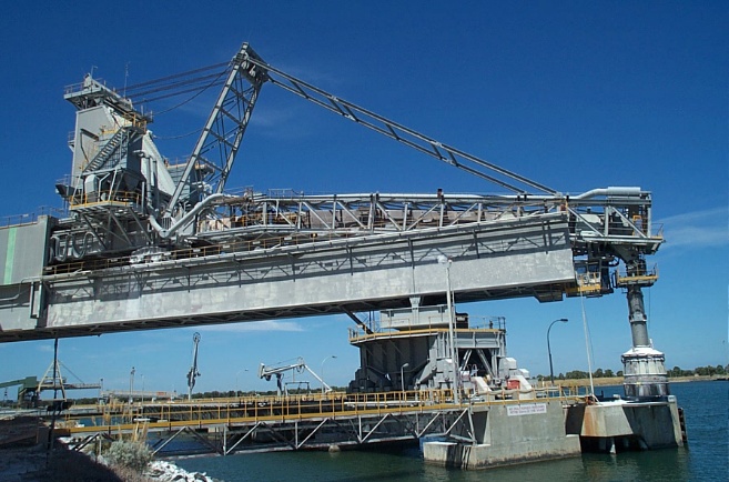 Linear bridge type shiploader installed on wharf infrastructure beside the water.