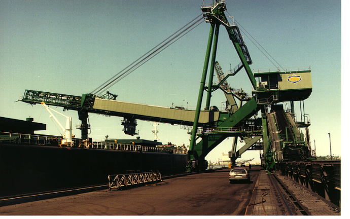Diagram of a long travelling shiploader with a fixed boom and internal shuttle extending over a vessel.