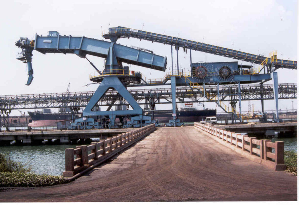 Portal slewing and shuttling shiploader with conveyor boom and rail-mounted portal structure on a wharf.