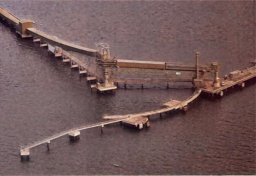 Aerial view of a single radial shiploader and curved wharf structure extending over the water.
