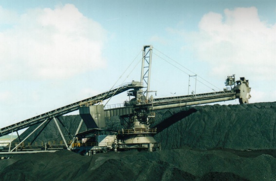 Rail-mounted stacker reclaimer with bucketwheel boom operating at a coal stockpile.